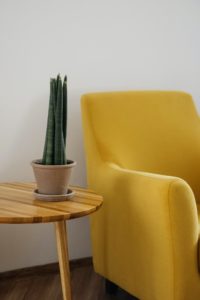 Żółty fotel ze stolikiem i rośliną. 